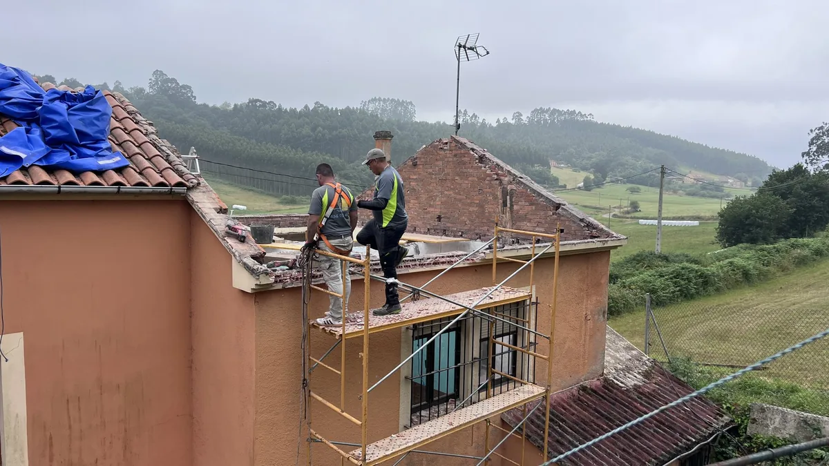 Reforma de tejado en Asturias: operarios rehabilitando la cubierta y el hastial de una vivienda.